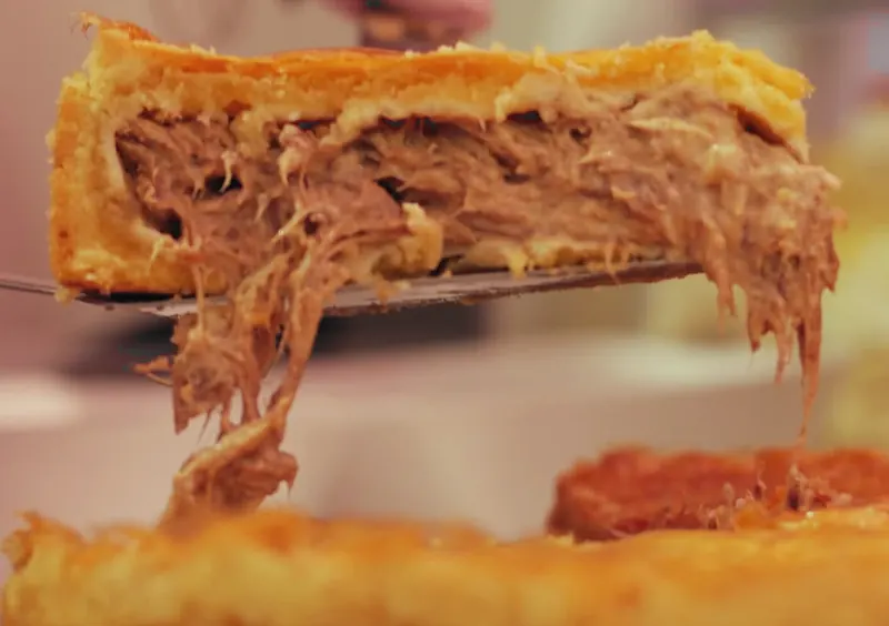 Espátula levanta uma fatia de torta e o recheio de carne desfiada solta fios
