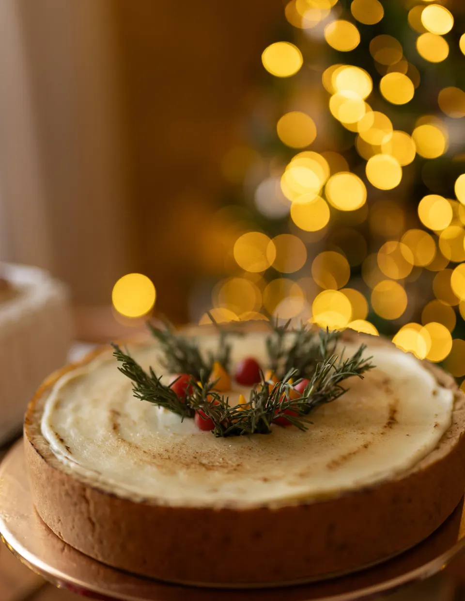 Torta salgada inteira, com creme dourado no maçarico e coroa de alecrim, diante da árvore de Natal com as luzes acesas