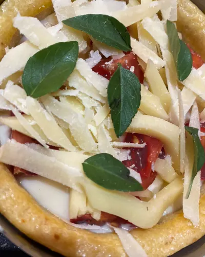 Tortinha aberta com tomate, lascas de queijo e folhas de manjericão